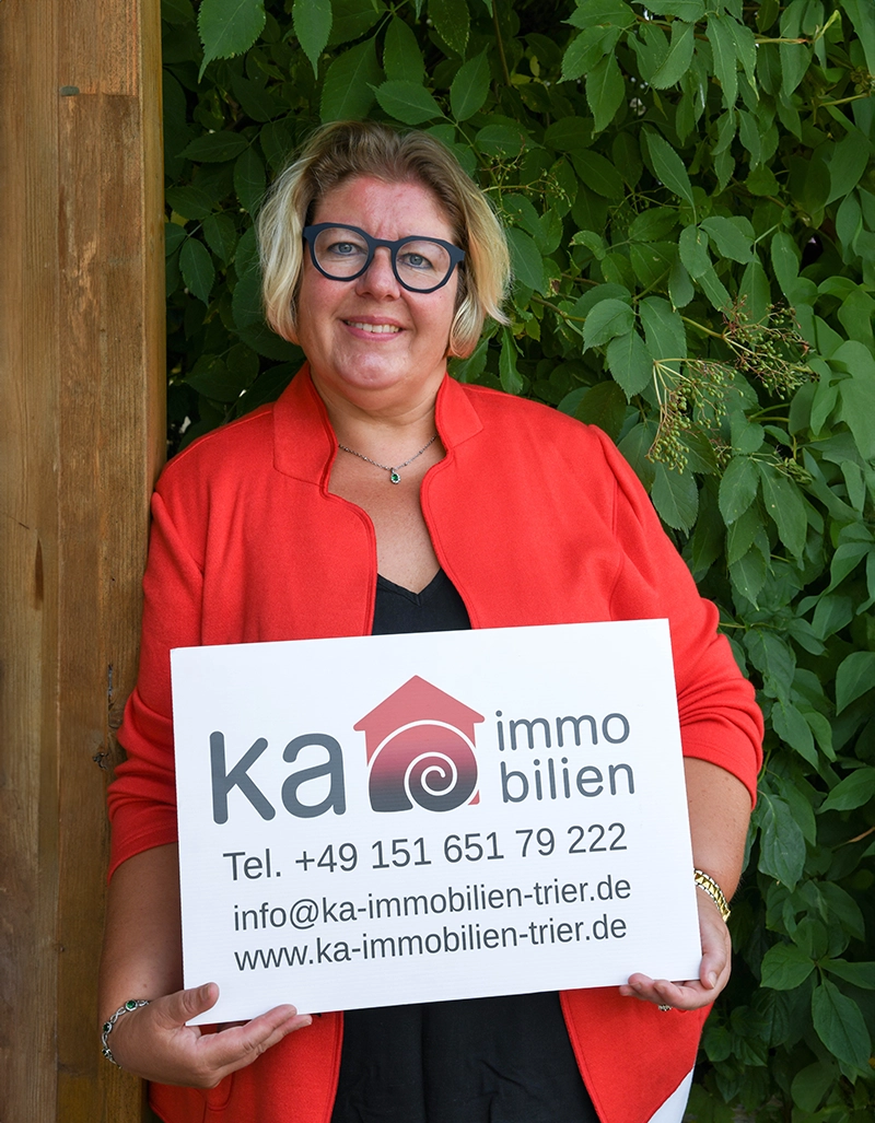 Annett Kreß hält Firmenschild von Ka Immobilien Trier mit Kontaktdaten